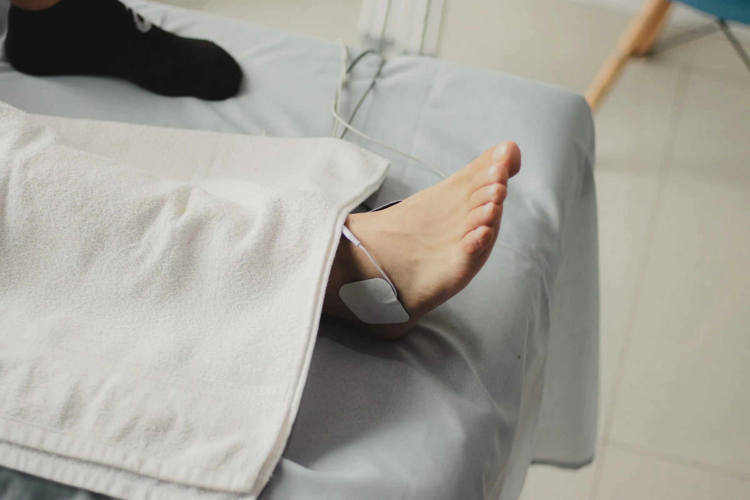 Pie de un paciente con electrodo de electroestimulación colocado sobre el tobillo, durante una sesión de electroterapia a domicilio