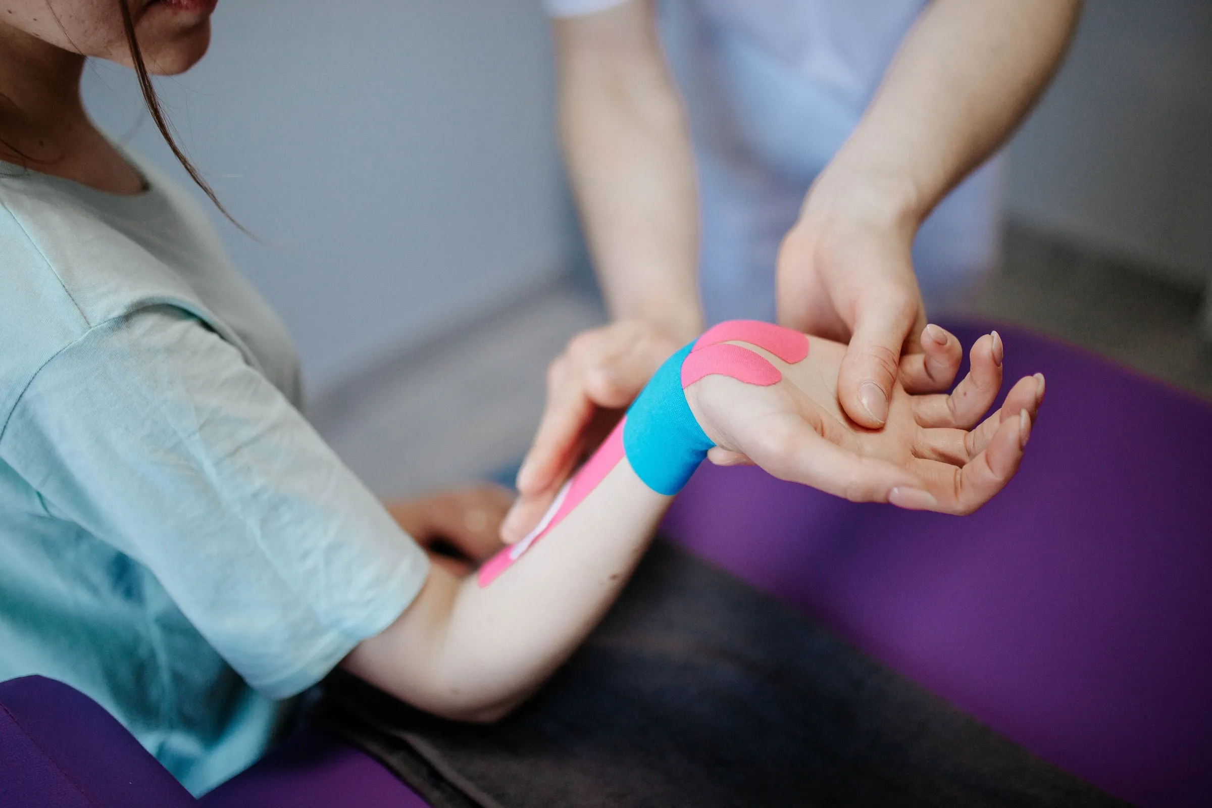 Kinesióloga aplicando cinta de vendaje neuromuscular en el antebrazo y muñeca de una paciente sentada