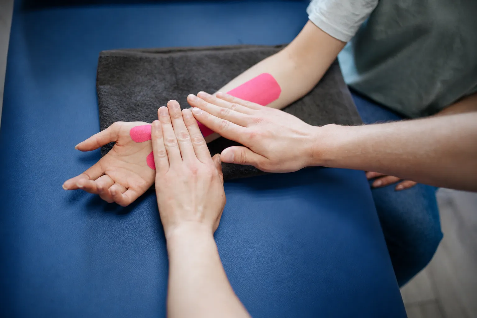 Kinesióloga aplicando vendaje neuromuscular en el antebrazo de un paciente